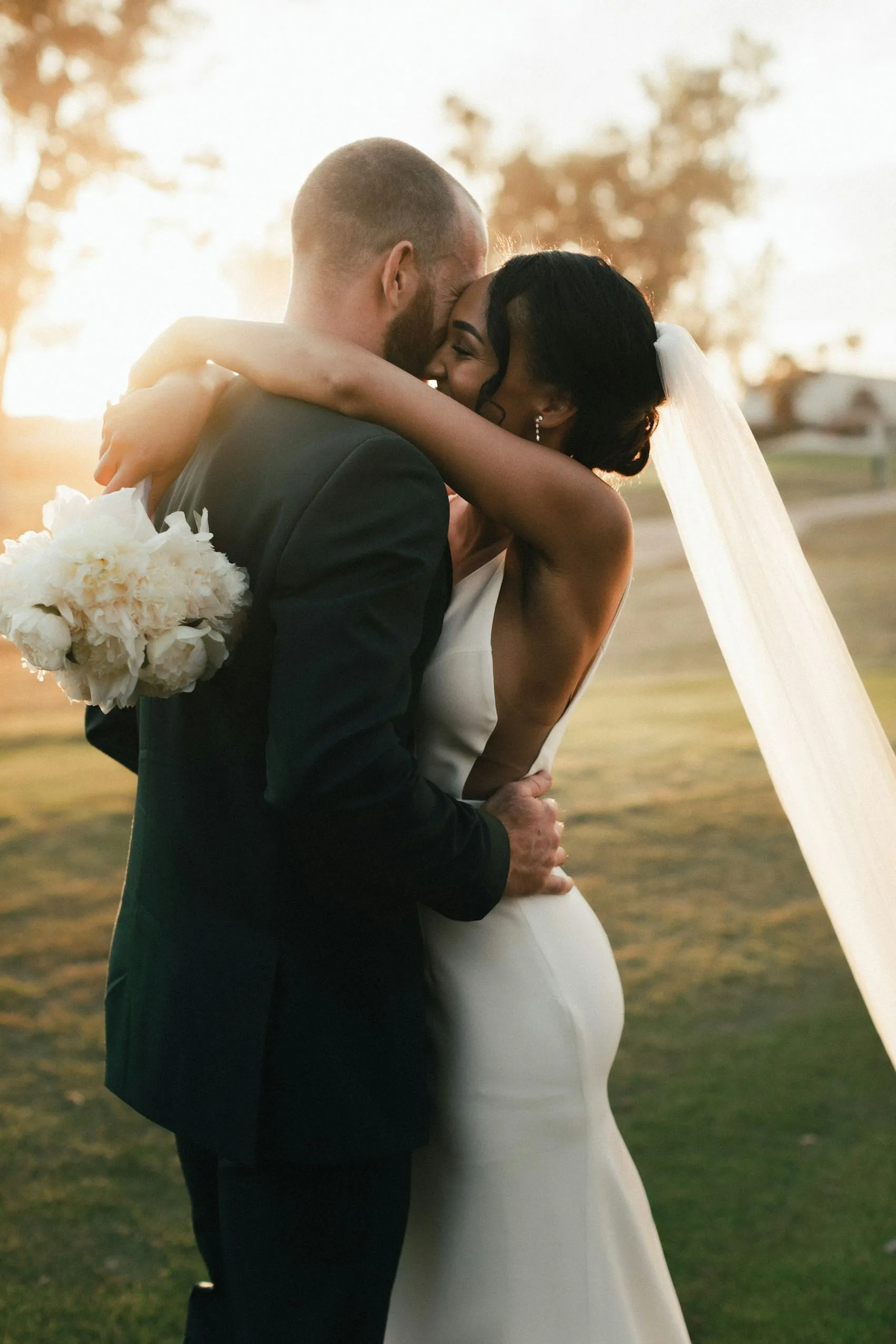A couple embracing in a golden field at sunset, veil lifting in the wind