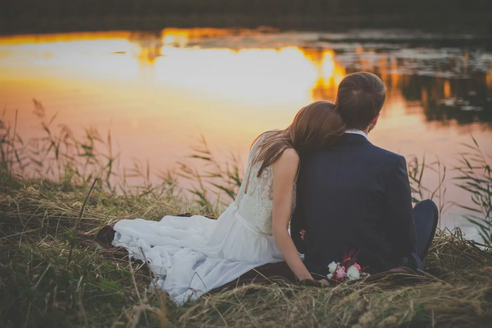 A couple sitting together beside water at sunset